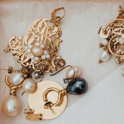 Various styles of gold and pearl earrings laid out on a beige, satin fabric.