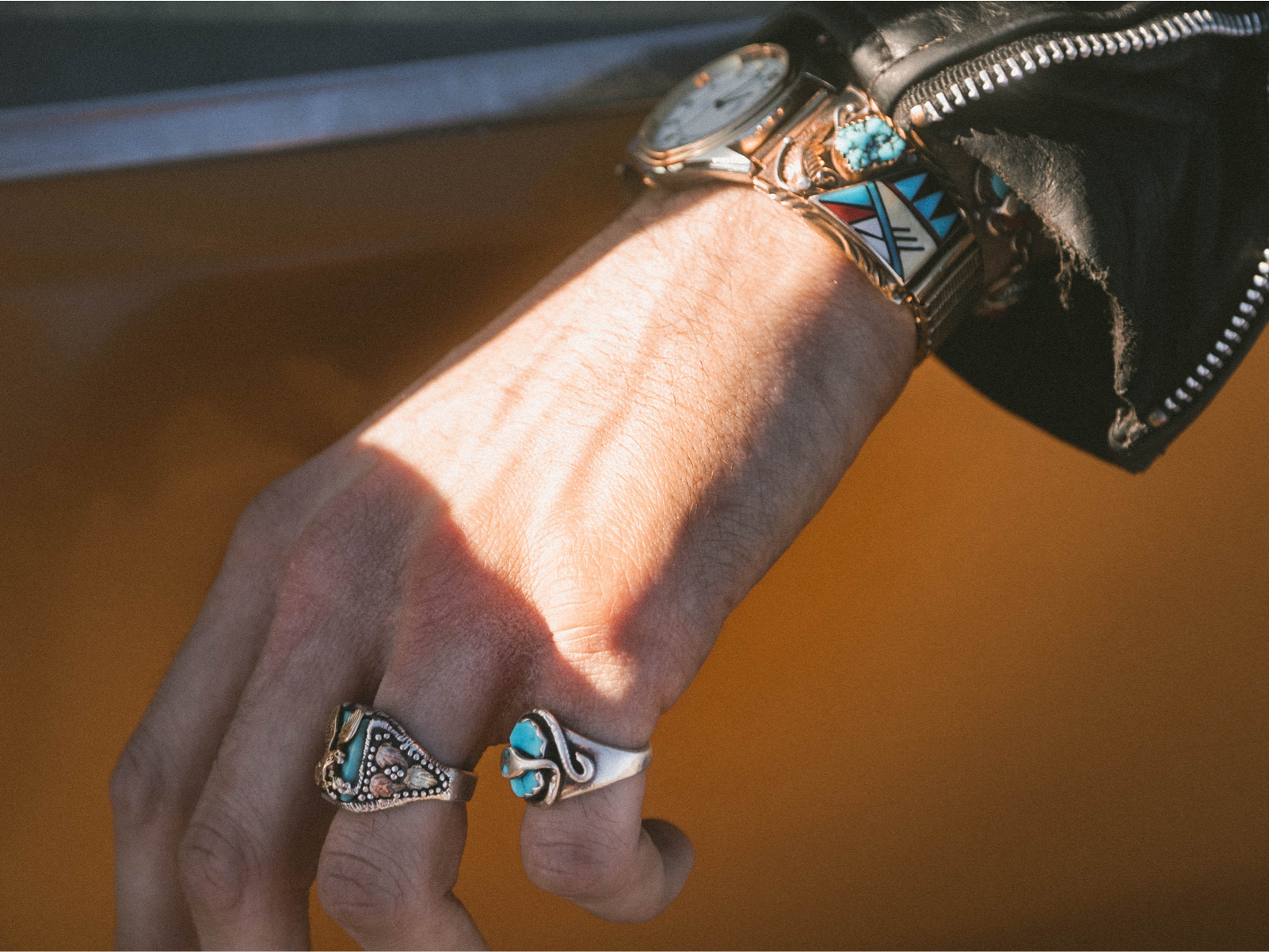 A woman's hand hanging outside of a yellow car window. She is wearing two silver rings with blue stones and intricate designs and a matching watch.