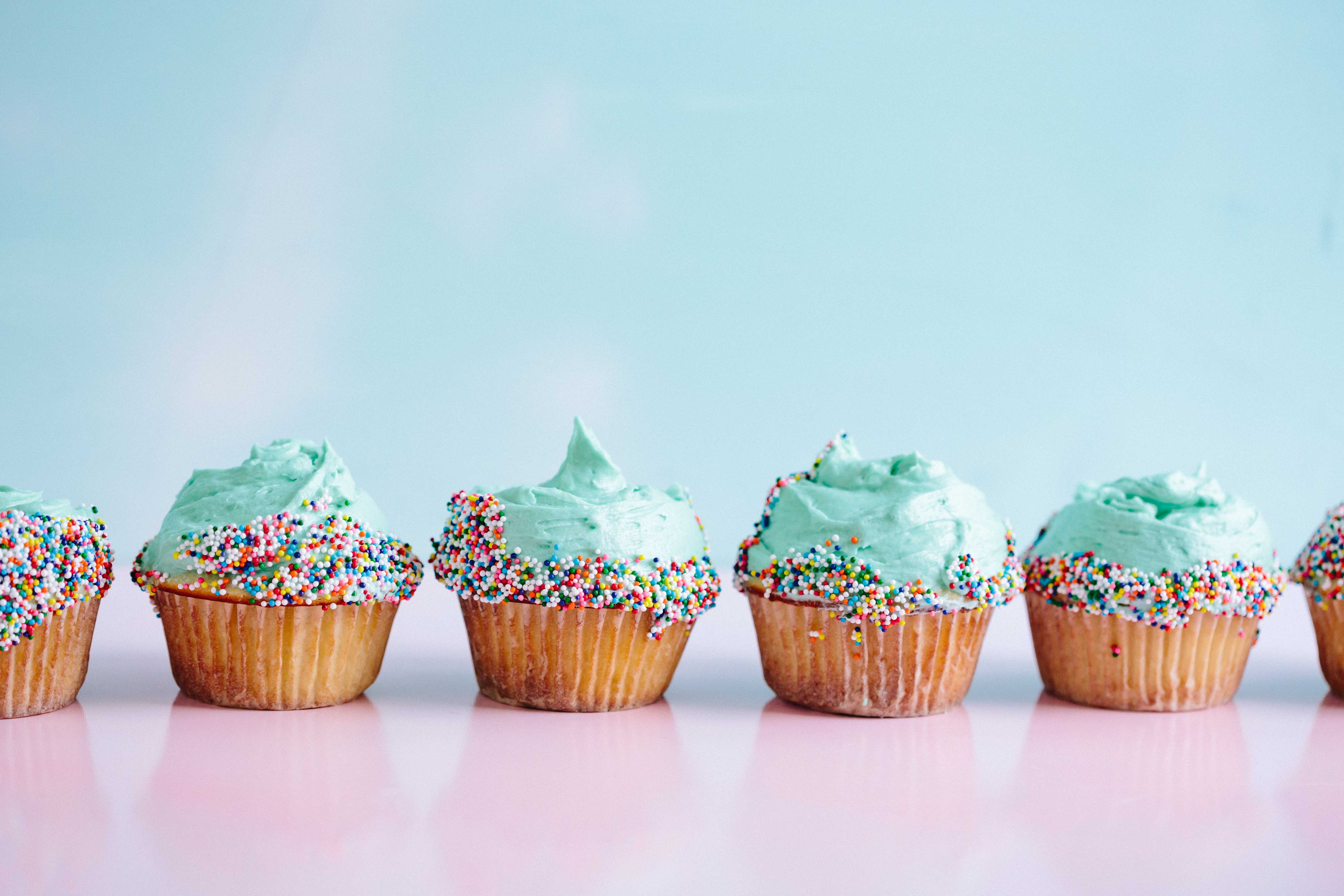 A row of vanilla cupcakes with mint green icing and sprinkles on top.