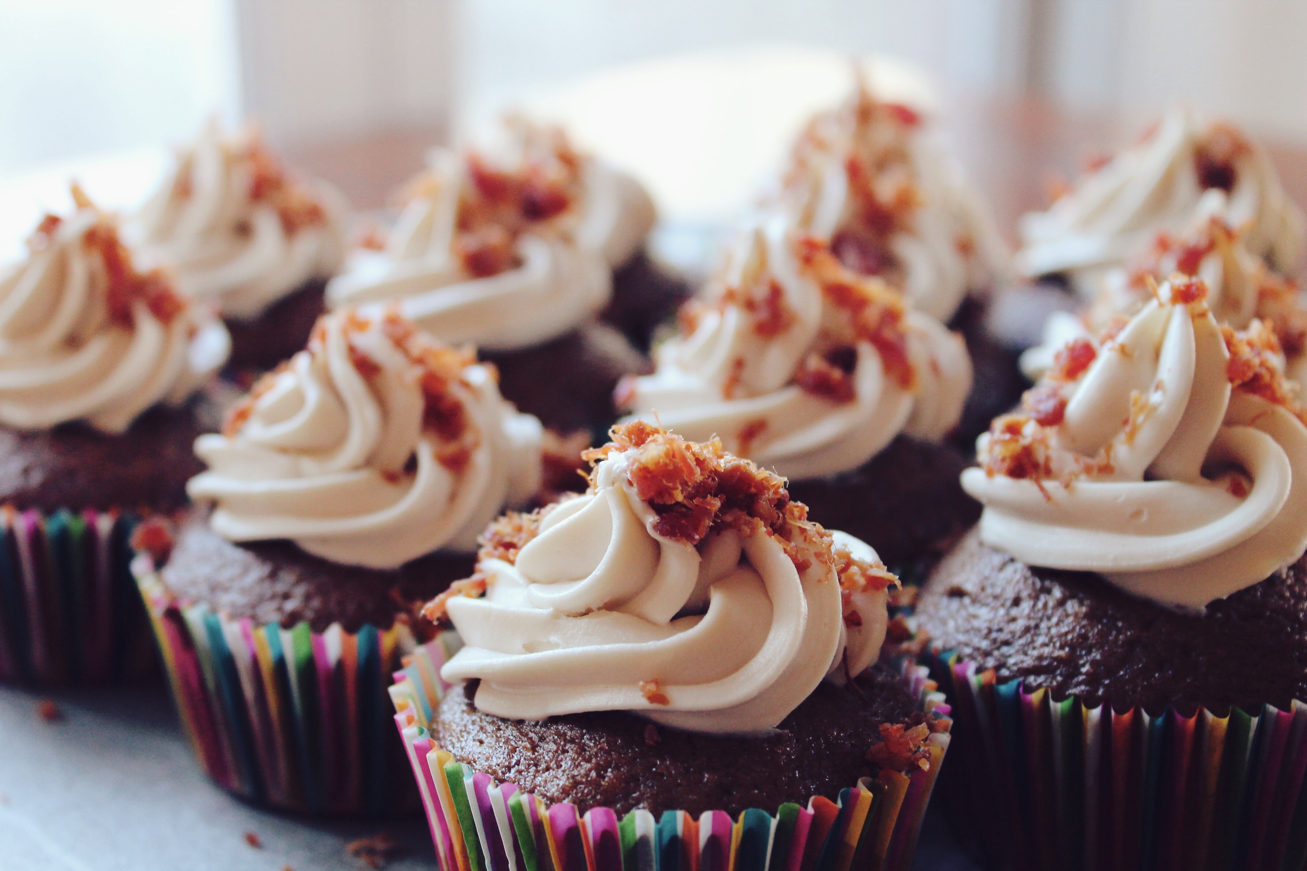 A bunch of chocolate cupckes with white icing and bacon bits on top.
