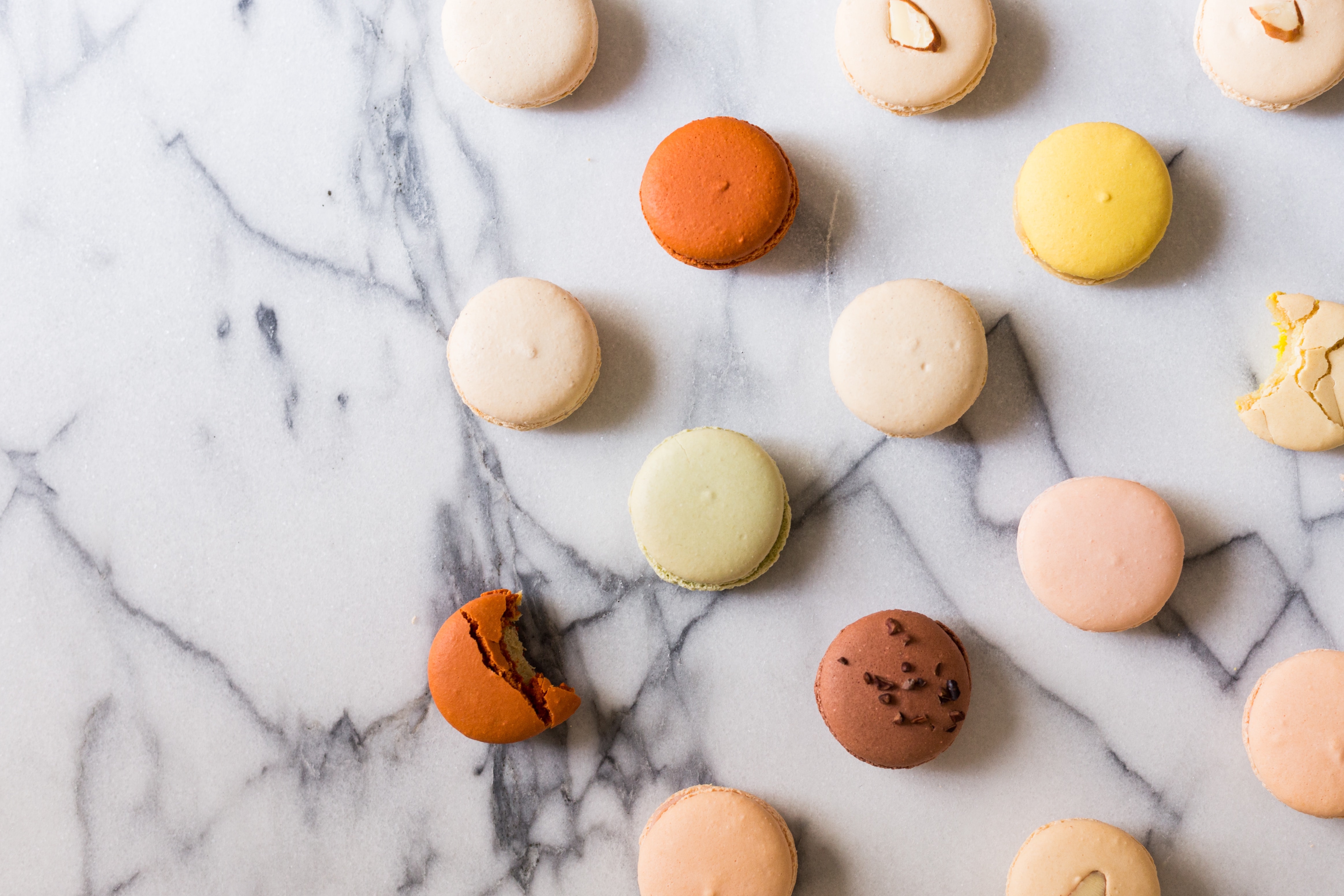 Various colours of macarons laid out in a staggered pattern on white marble.